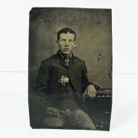 Antique Tintype Photo: Man sitting, with a boutonniere in his jacket. The hand resting in his lap is very dark: Front View - Click to enlarge