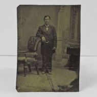 Antique Tintype Photo: Man, standing, leaning one arm on the back of leather back chair with padded arms and wood frame: Front View