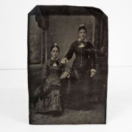 Antique Tintype Photo: Two women - One sitting, One standing. Bows on their dress collars and flower on top of their head: Front View